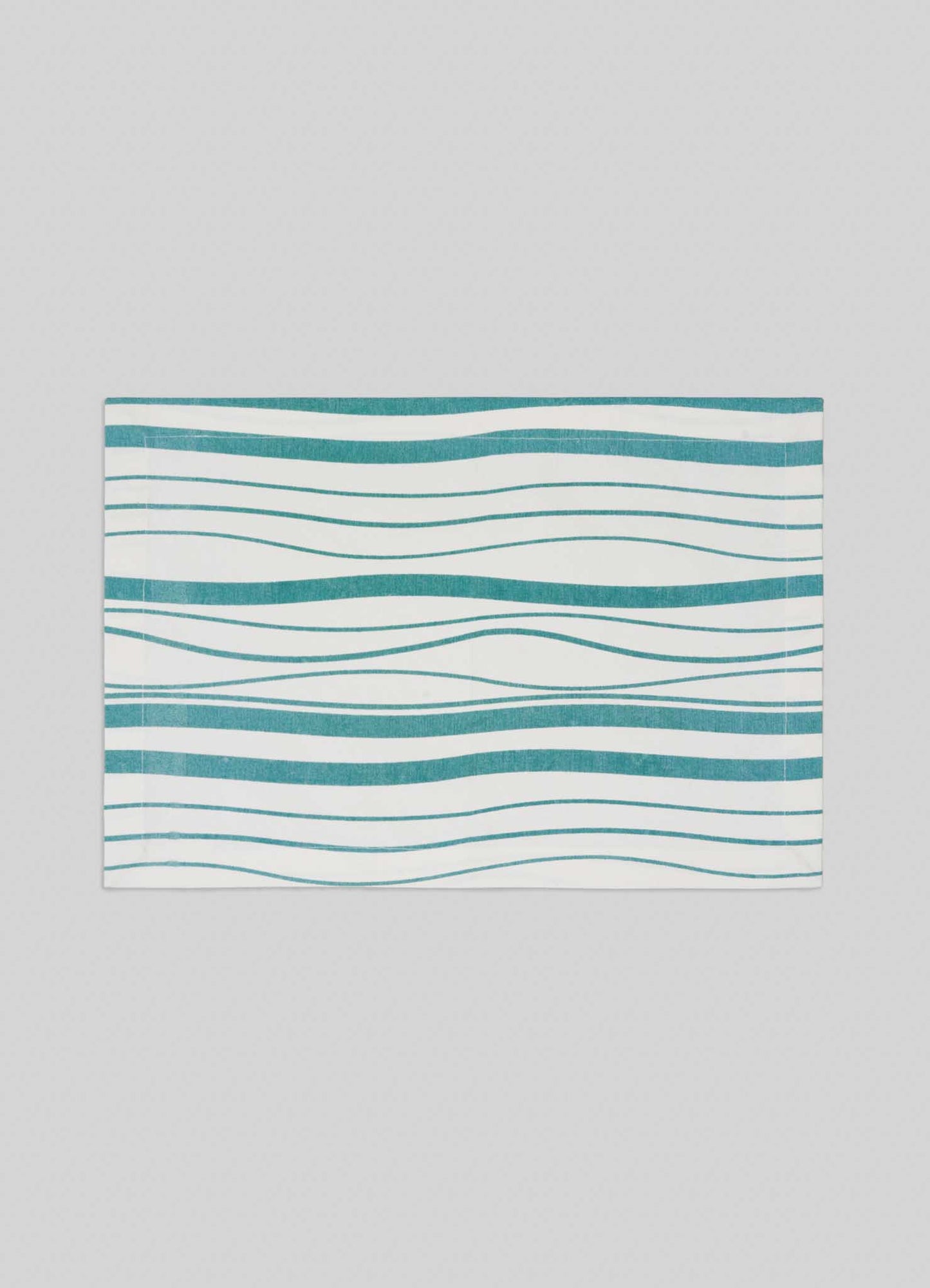 The Viya Madras Check Aqua Placemats (Set of 4) feature a white background with teal wavy horizontal lines in varying thicknesses, creating an abstract, flowing pattern inspired by Indian artistry. Shown centered on a light gray backdrop.