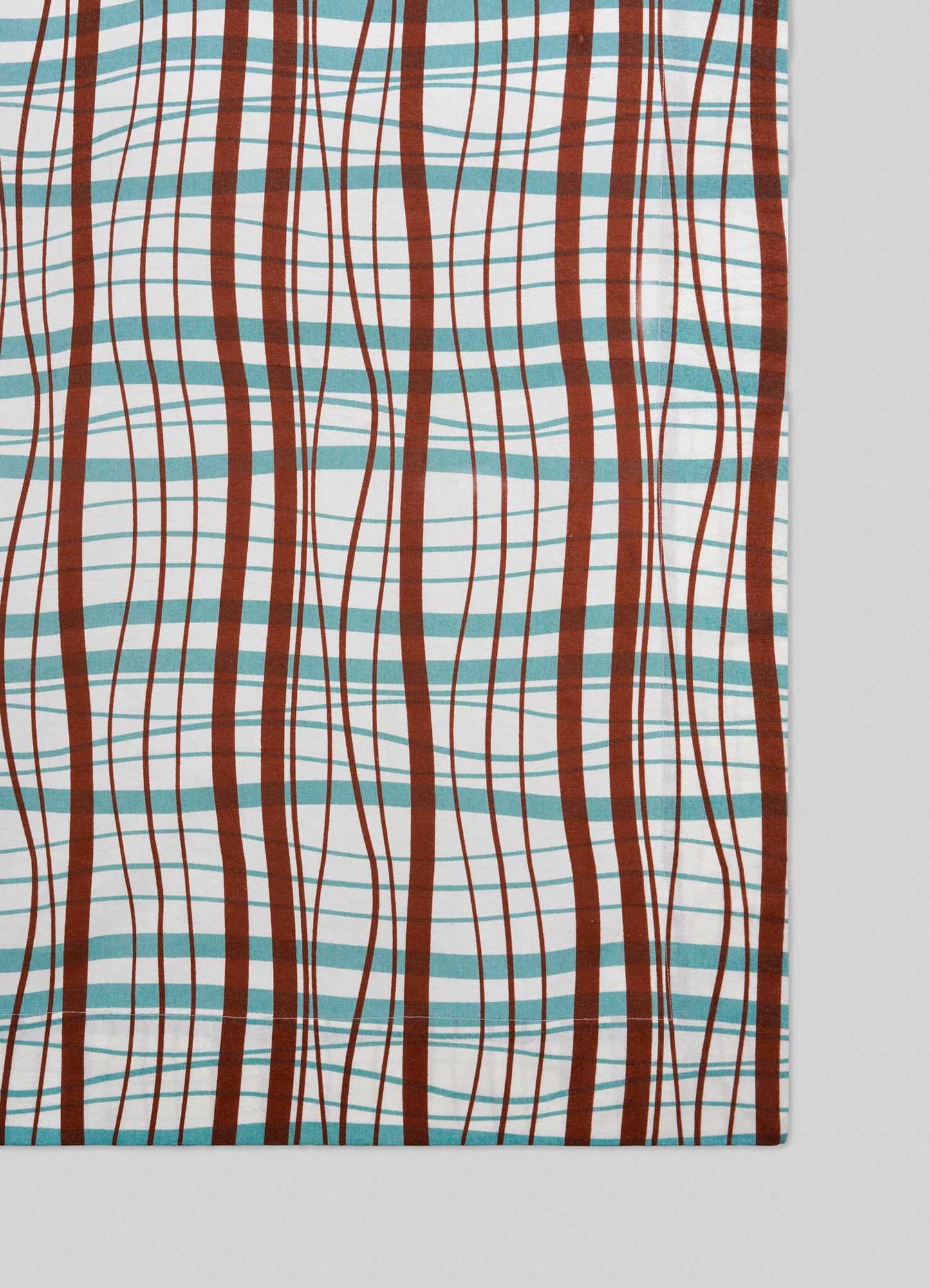 The Viya Madras Check Aqua & Rust Table Cloth features a rectangular design with wavy brown, teal, and red lines forming a modern take on classic Indian Madras checks, displayed diagonally on a light gray surface.