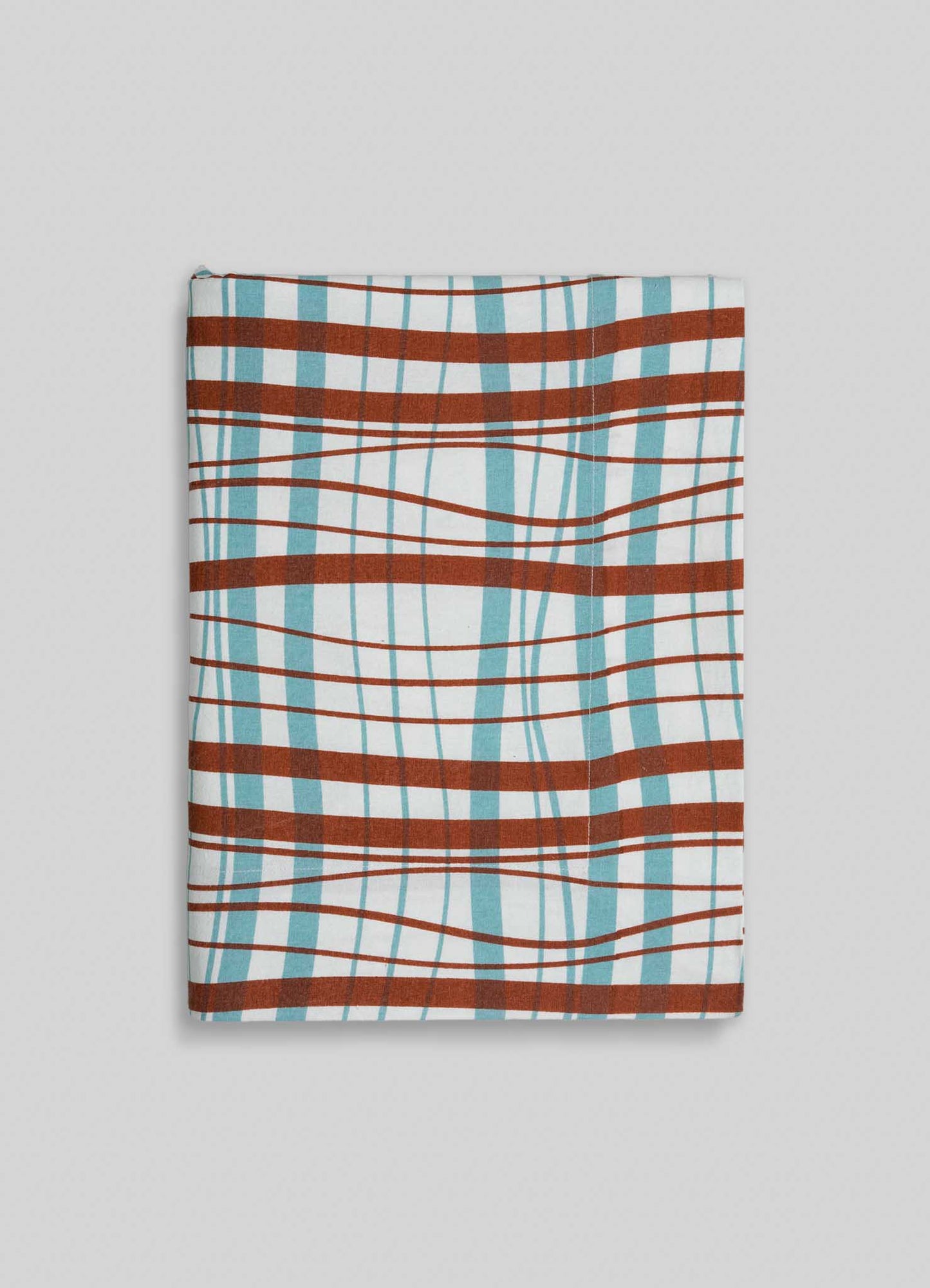 The Viya Madras Check Aqua & Rust Table Cloth showcases a folded fabric with an aqua and rust distorted plaid pattern, featuring curved and wavy lines, set against a light gray background.