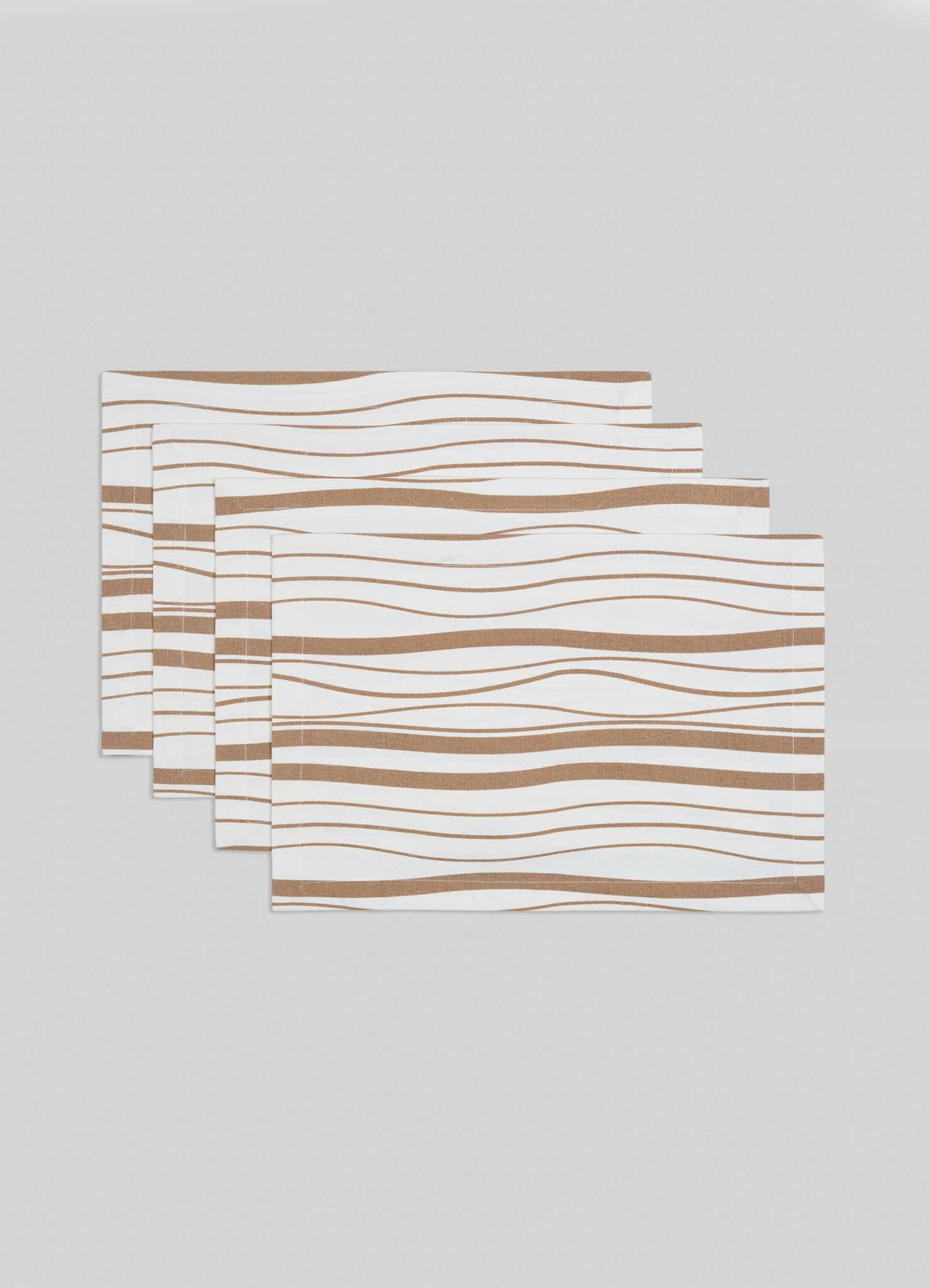 The Viya Madras Check Beige Placemats, set of 4, feature a white base with wavy brown lines inspired by contemporary Indian textiles, shown stacked in a staggered arrangement on a light gray surface.
