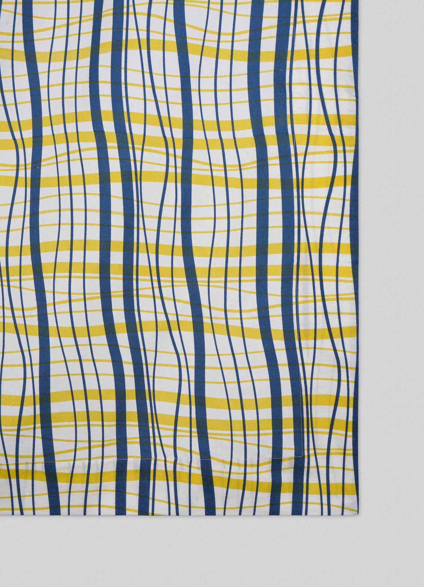 The Viya Madras Check Blue & Yellow Table Cloth features a wavy, irregular plaid of blue and yellow lines on white, shown on a light gray surface.