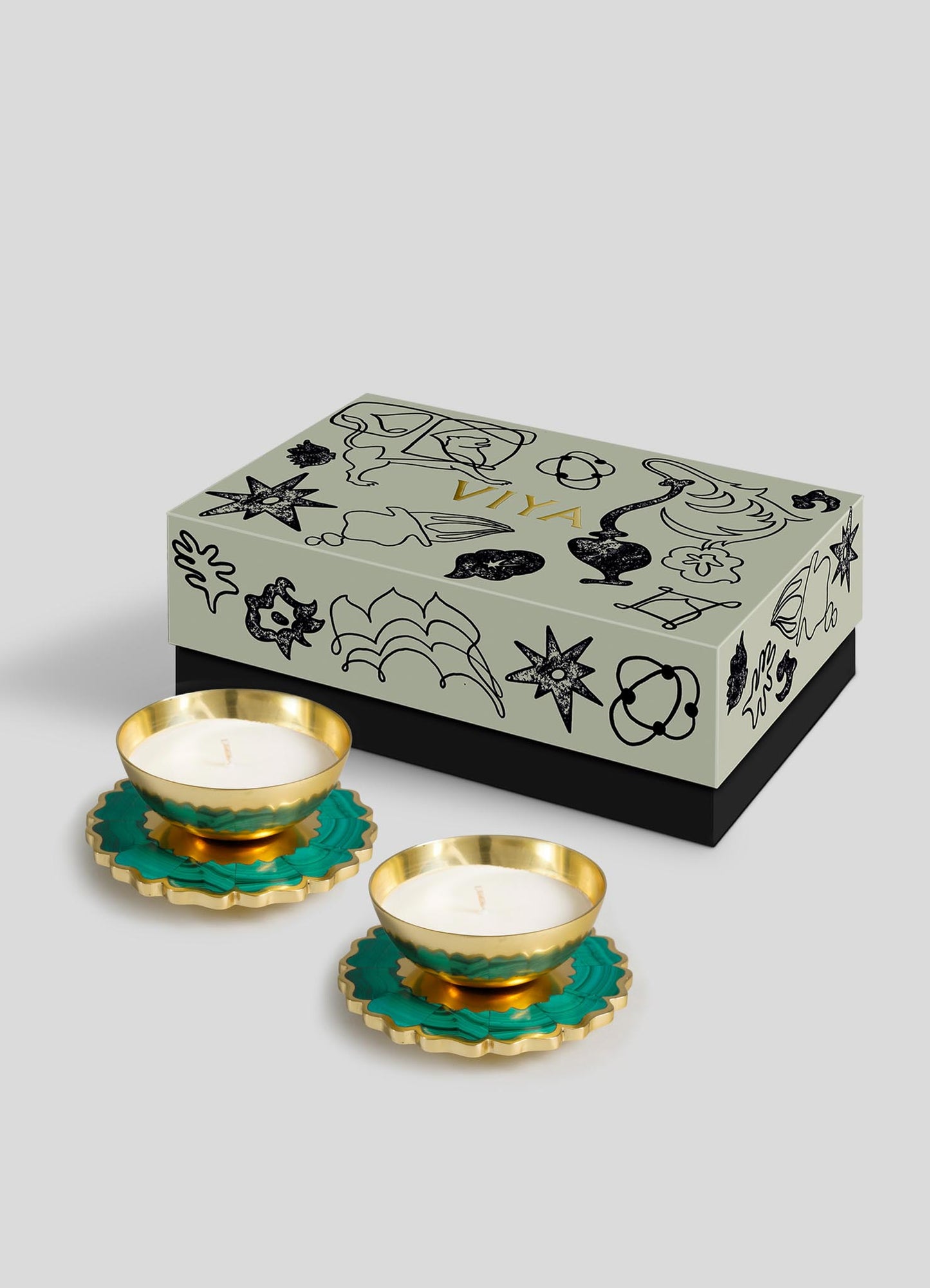 The Viya Mystical Marigold Green Scented Candle Diya Small Set of 2 features brass tealight holders with green and gold floral bases and white candles, displayed before a decorative gift box on a light gray background.