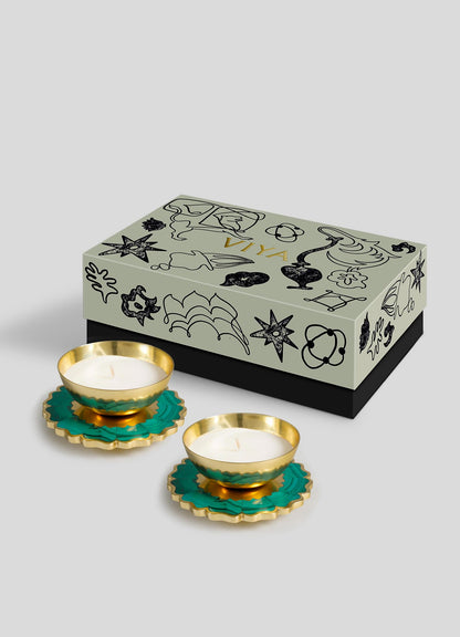 The Viya Mystical Marigold Green Scented Candle Diya Small Set of 2 features brass tealight holders with green and gold floral bases and white candles, displayed before a decorative gift box on a light gray background.