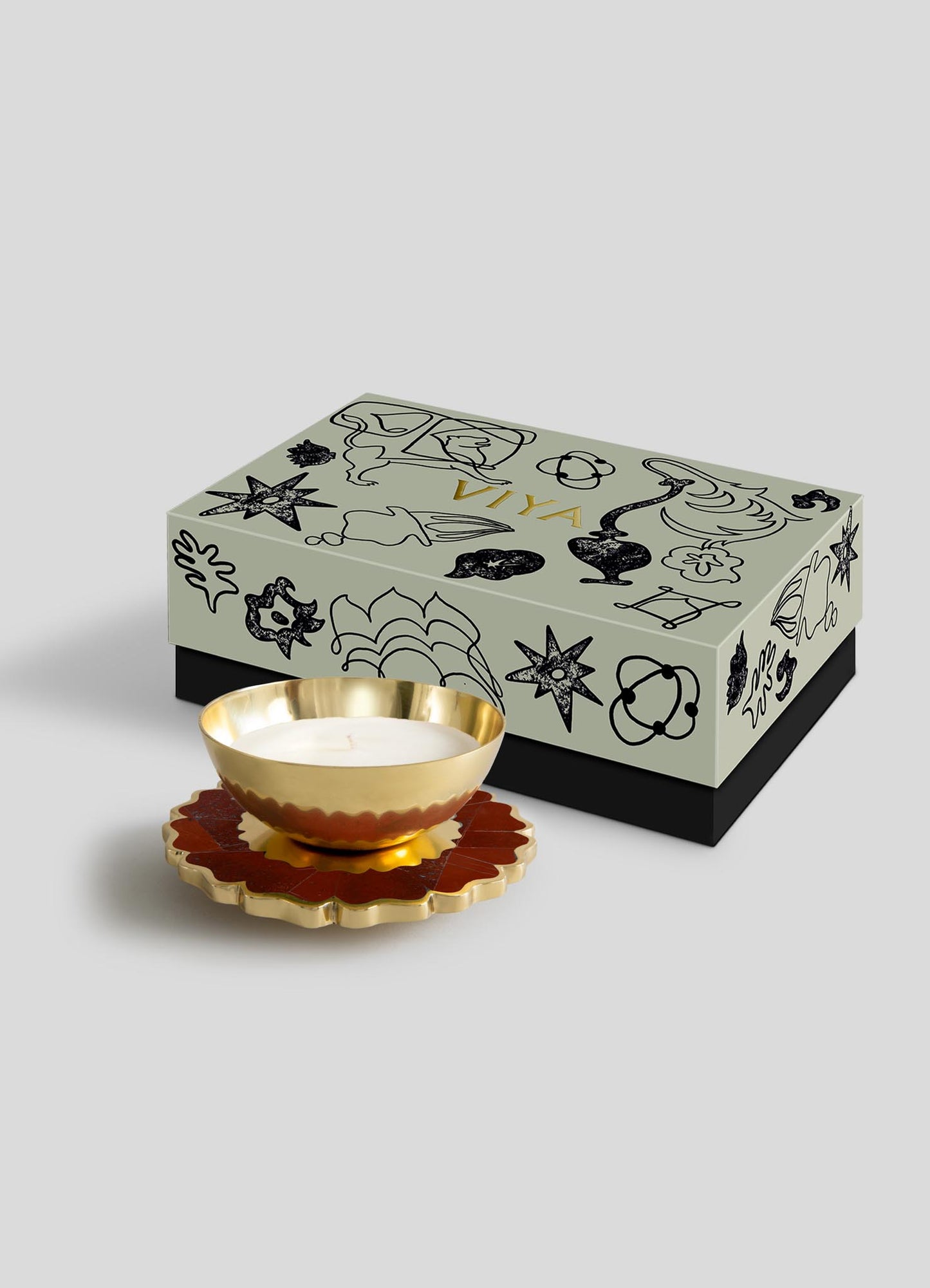 The Viya Mystical Marigold Red - Scented Candle Diya Large features a decorative box with black abstract botanical patterns inspired by Pichwai art, paired with a gold candle holder and floral coaster—a perfect modern heirloom for your space.
