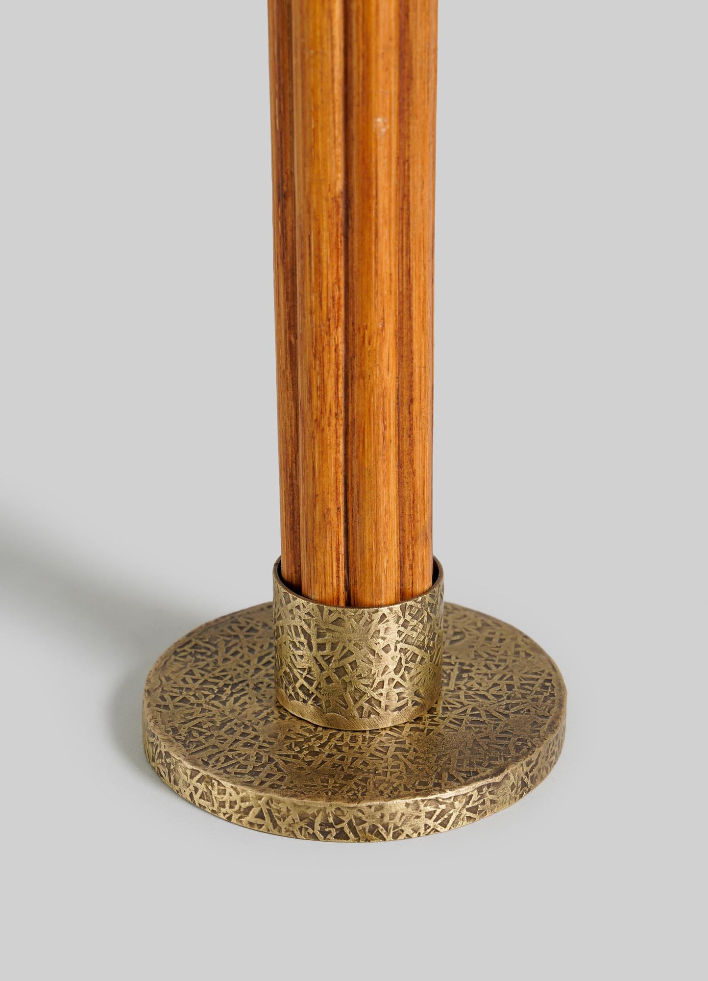 The Namsai Candle Holder Large by VIYA features a wooden pole with a decorative round brass base, adorned with intricate cane weaving and engraved patterns, displayed against a plain light gray background.