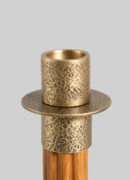 A close-up of the VIYA Namsai Candle Holder Large—an elegant, textured cylindrical brass piece with a wide flat base, mounted on a vertical wooden rod, set against a plain gray background.