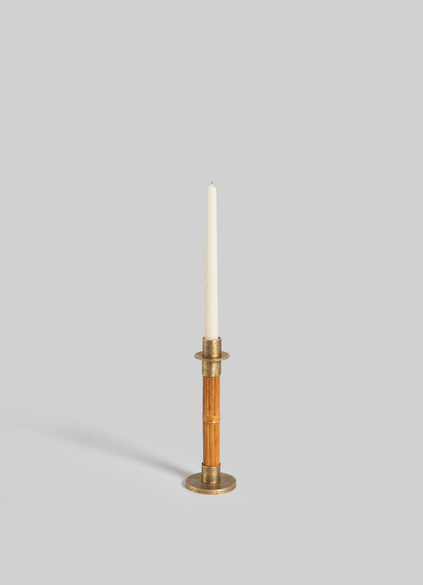 The VIYA Namsai Candle Holder Small features brass and wood with a textured round base, brass trimmings, and a ring detail. Shown holding a white taper candle against a plain light gray background.