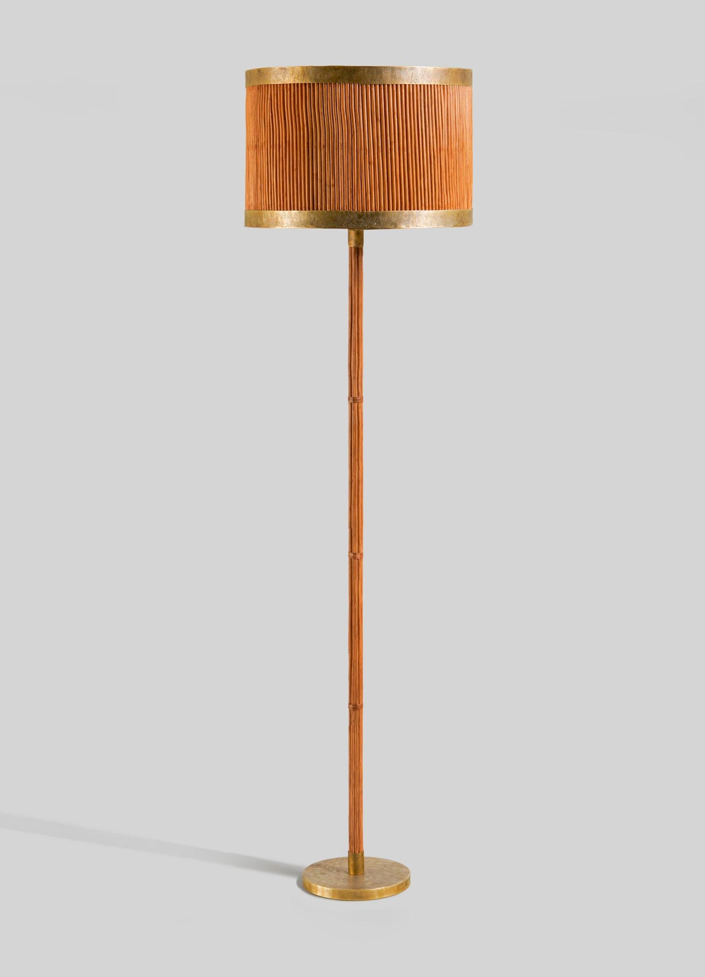 The VIYA Namsai Floor Lamp Round features a pleated orange lampshade, slender wooden pole, and circular gold base with brass accents, shown against a plain light grey background.