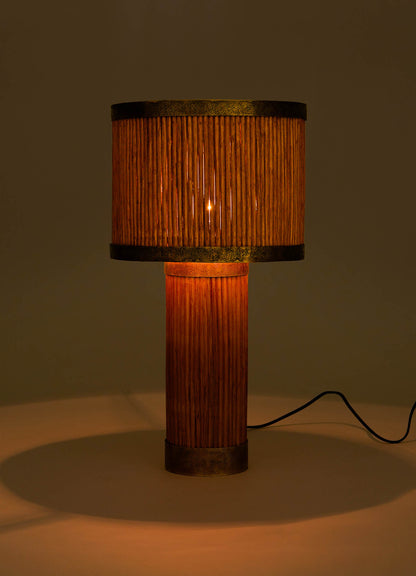 The VIYA Namsai Table Lamp Round features a cylindrical base and shade of vertical wooden slats inspired by cane weaving, emitting a warm amber glow with a black power cord extending from the base.