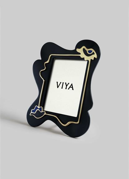 The Nazar Black Photo Frame by VIYA stands upright on a gray surface, featuring an irregular black shape with gold and blue accents. Inside is a white placeholder with "VIYA" printed at the center.