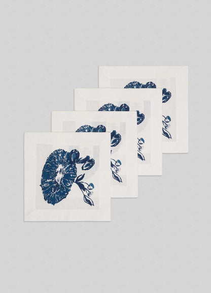 The Viya Orchard Blue Cocktail Napkins, a set of four white napkins with blue botanical mushroom and leaf prints inspired by an Indian fruit orchard, are arranged in a staggered stack on a light gray background.