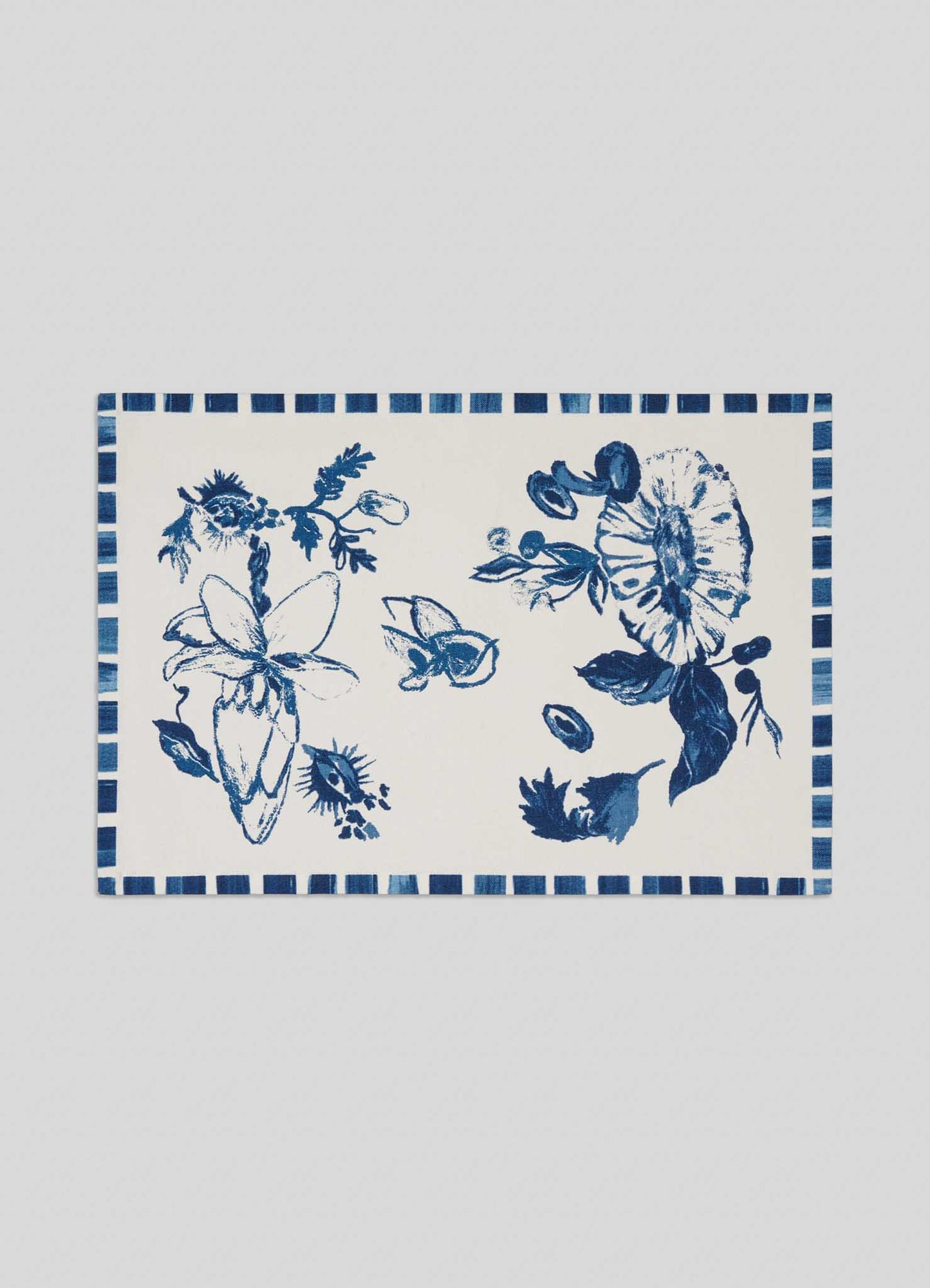 The Viya Orchard Blue Placemats - Set of 4 feature a rectangular white design with hand-painted blue floral patterns and a striped border, inspired by Indian fruit orchard motifs like wood apple and pomegranate.