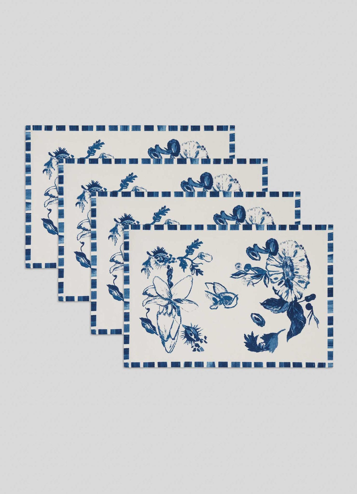 The Viya Orchard Blue Placemats - Set of 4 feature a blue and white floral design with a blue checkered border, inspired by the colors of wood apple and Indian pomegranate orchards.