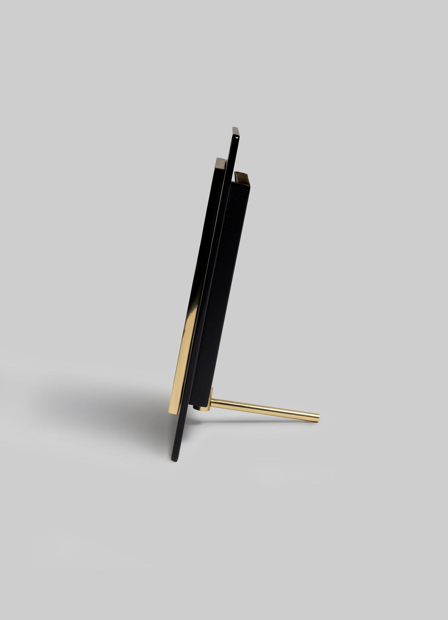 The VIYA Plaza Photo Frame, featuring a minimalist black and gold Art Deco design, is displayed upright from the side on a gray background with its slim support rod visible at the back.