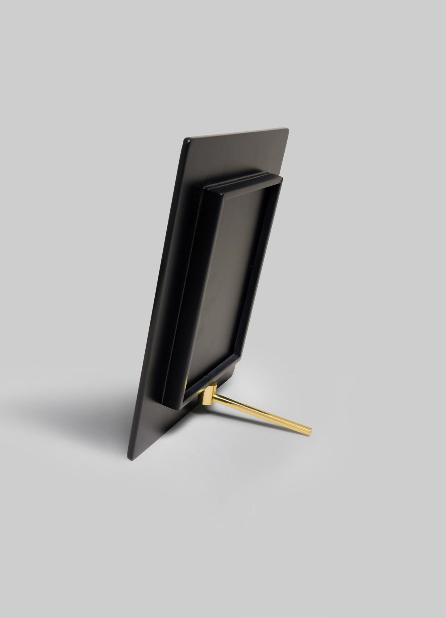 The VIYA Plaza Photo Frame, rectangular and black, is displayed from the back. Its gold metal stand channels Art Deco style inspired by old Bombay cinema halls, all set against a plain light gray background.