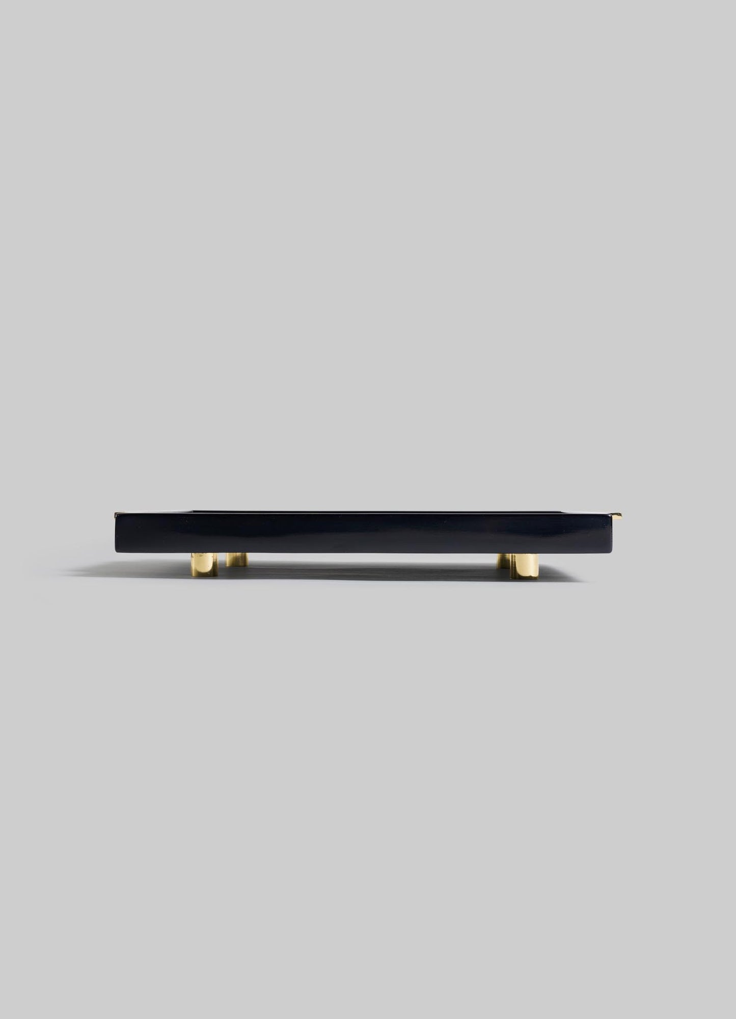 The Plaza Towel Tray by VIYA, a sleek rectangular black piece with gold feet, captures the Art Deco style of Bombay’s historic cinema halls, shown from a low side angle against a plain light gray background.