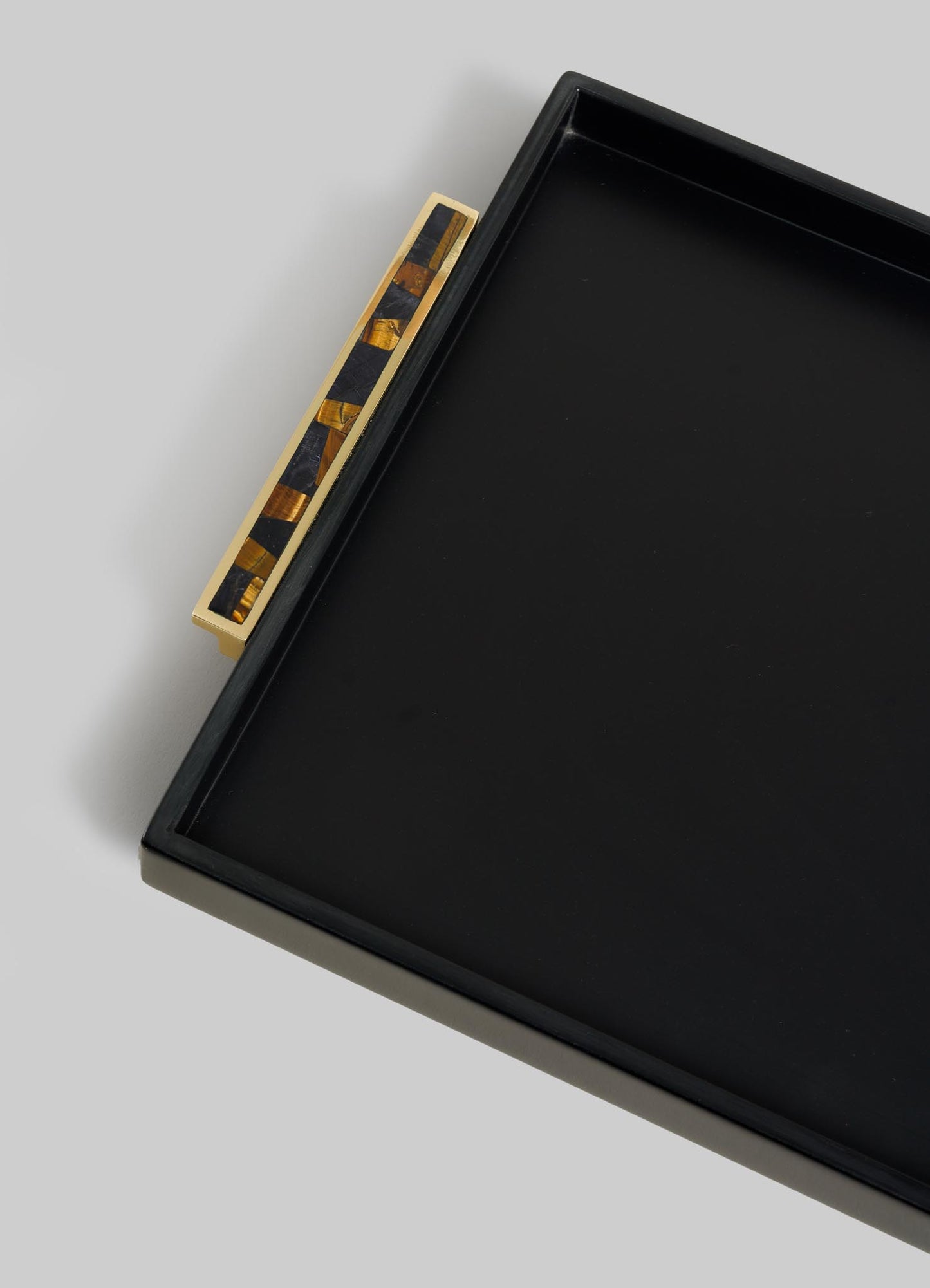 A close-up of the VIYA Plaza Towel Tray—a rectangular black tray with a gold and tortoiseshell-patterned handle inspired by Art Deco Bombay cinema halls—photographed on a light gray background.