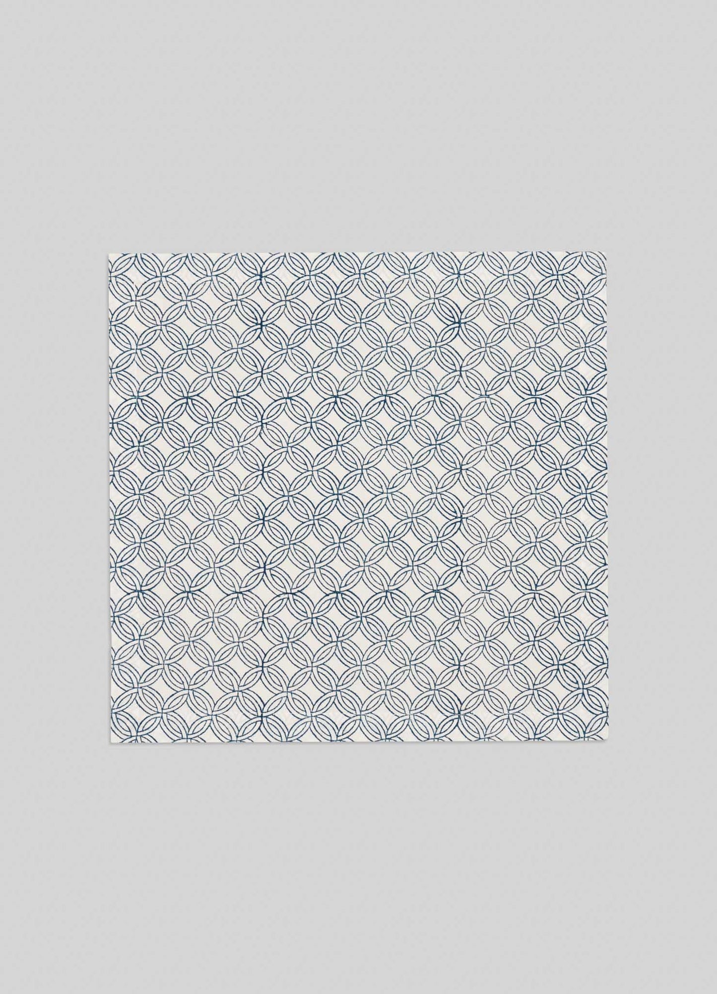 The Viya Paigah Navy Napkins (Set of 4) feature a square design with blue interlocking circle patterns inspired by Indo-Islamic paigah jaalis on a white background, shown against a plain light gray surface.