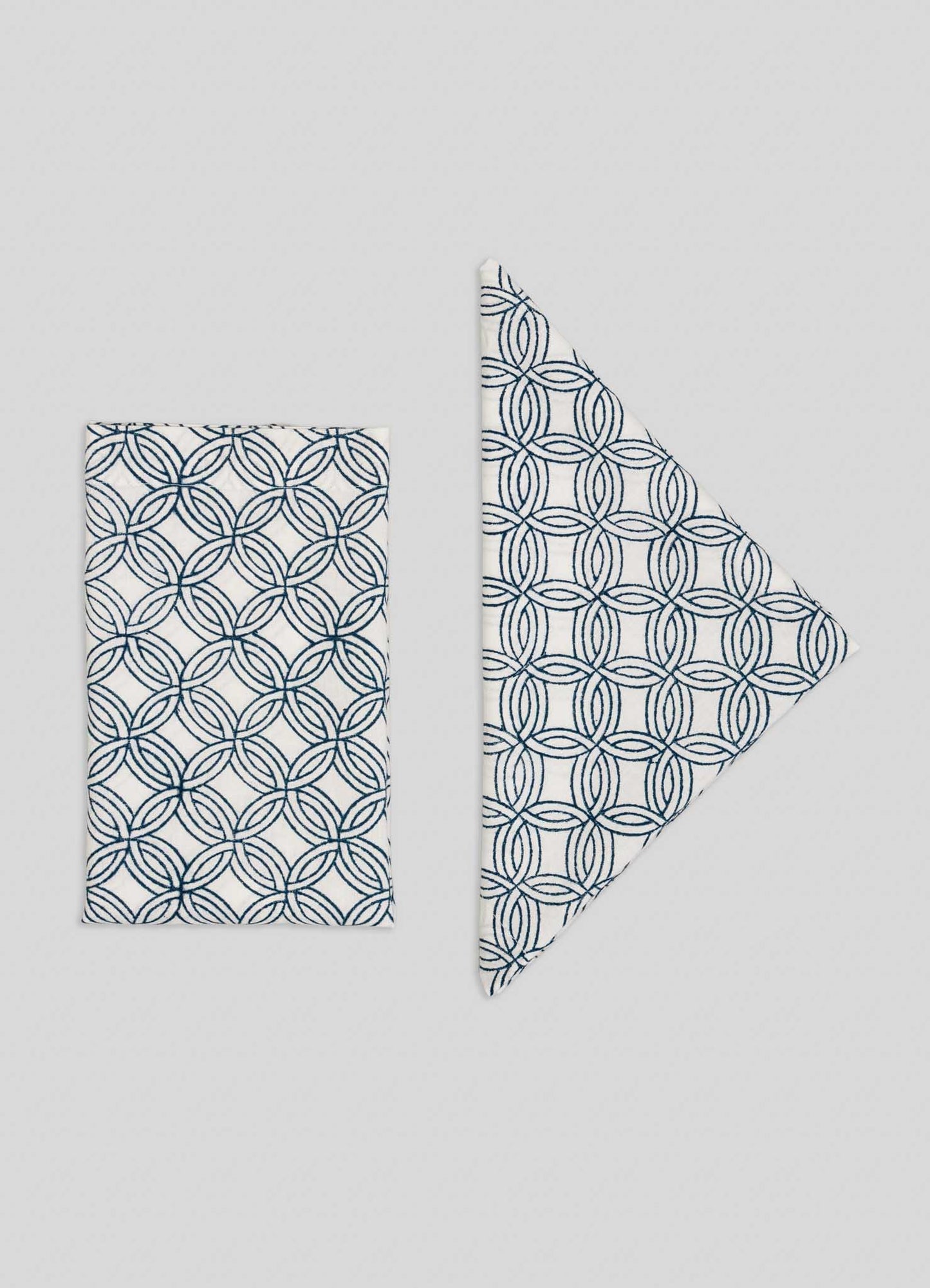 The Viya Paigah Navy Napkins - Set of 4 showcase a blue geometric circle pattern inspired by Hyderabad’s Indo-Islamic architecture, arranged in a slightly overlapping stack on a plain light gray background.