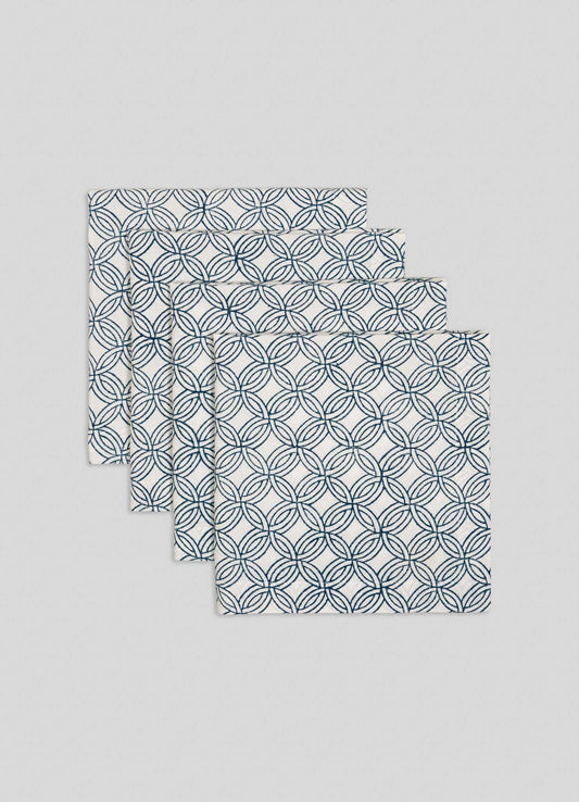 The Viya Paigah Navy Napkins - Set of 4, featuring a blue overlapping circle motif inspired by Hyderabad’s paigah jaalis, are neatly stacked in a fanned arrangement on a light grey background.