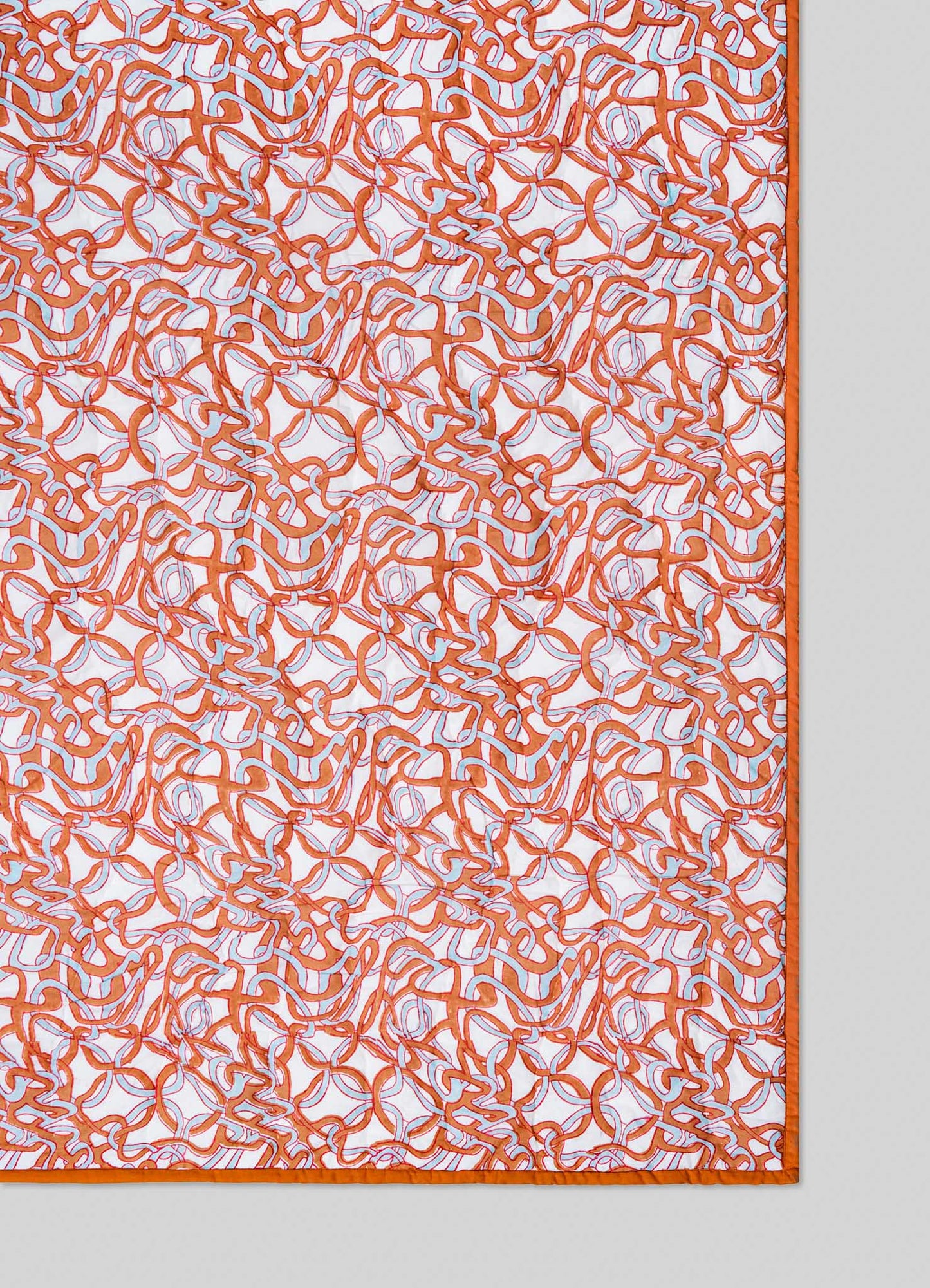 The Viya Paigah Orange & Blue Single Quilt showcases orange and white abstract lattice-inspired patterns with a matching orange border, displayed on a light grey background.