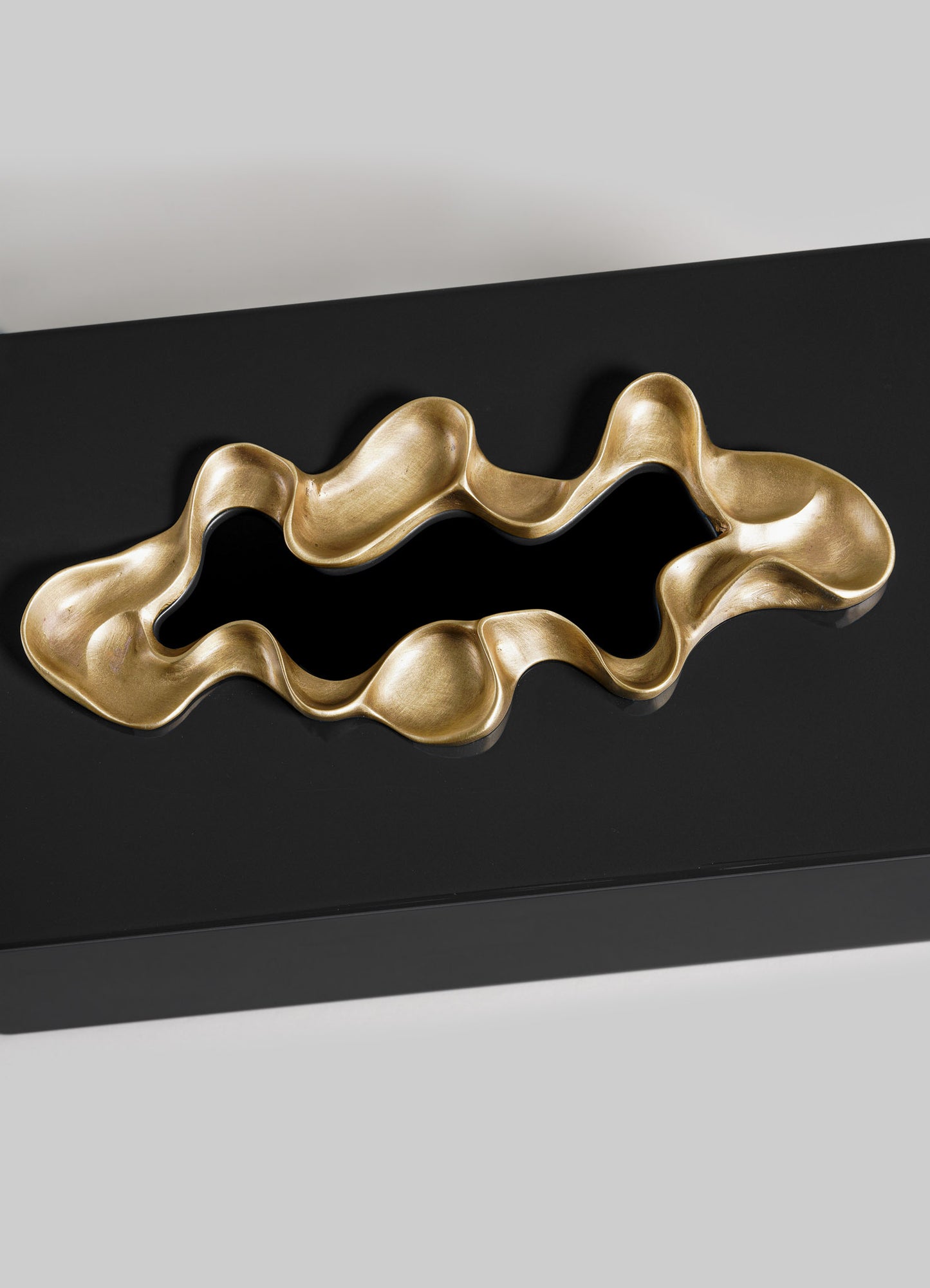 The Saffron Black Tissue Box Large by VIYA features a black rectangular design with an abstract gold metallic accent in the center, blending contemporary style with fluid, sculptural forms.