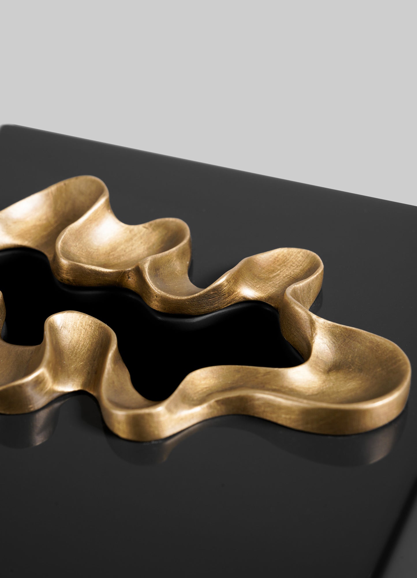 Close-up of the VIYA Saffron Black Tissue Box Small, a contemporary, gold-accented accessory resting on a glossy black surface against a plain grey background.