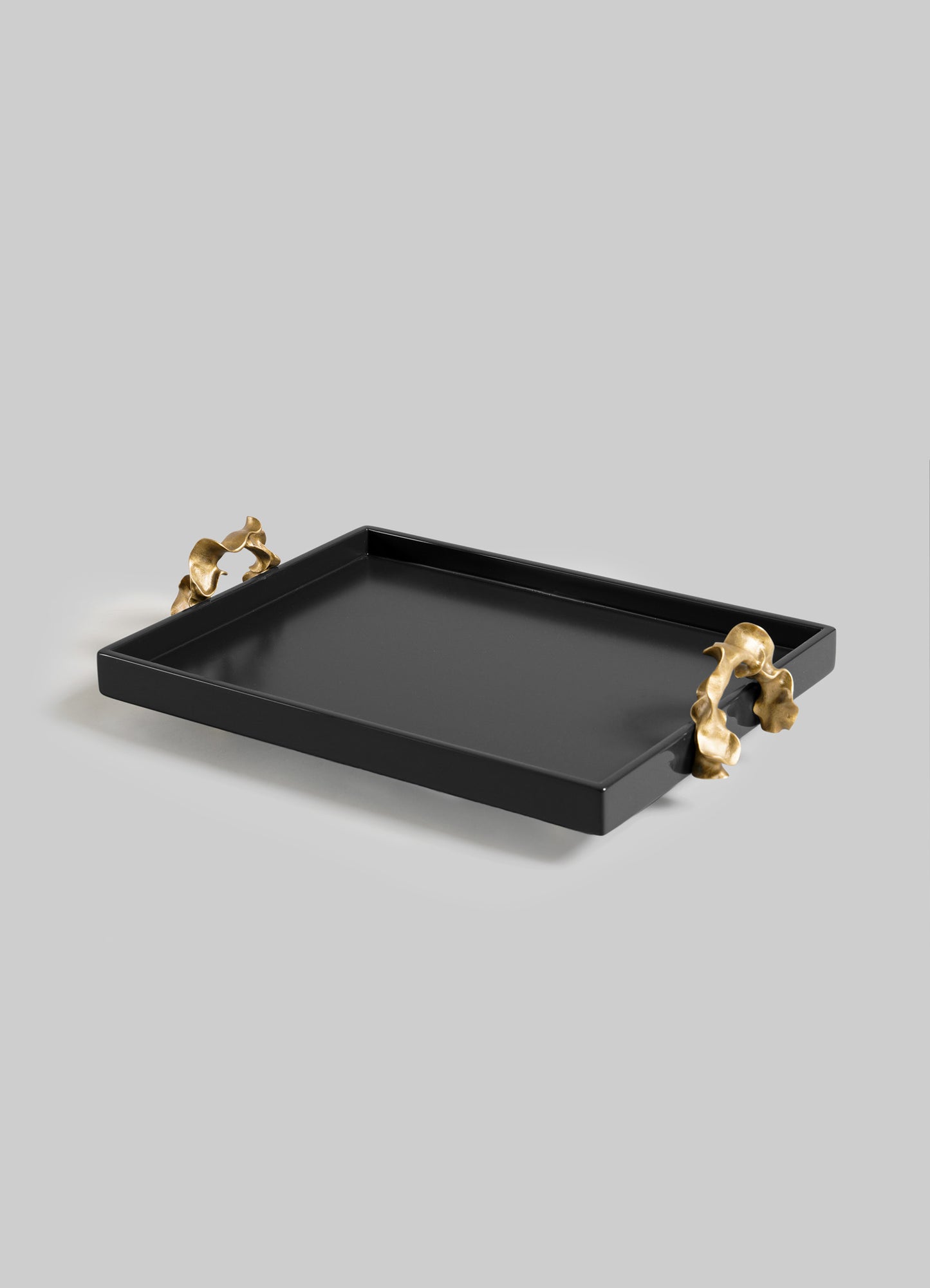 The VIYA Saffron Black Towel Tray features a rectangular black design with raised edges and two contemporary bronzed handles in abstract organic shapes, displayed against a plain light gray background.