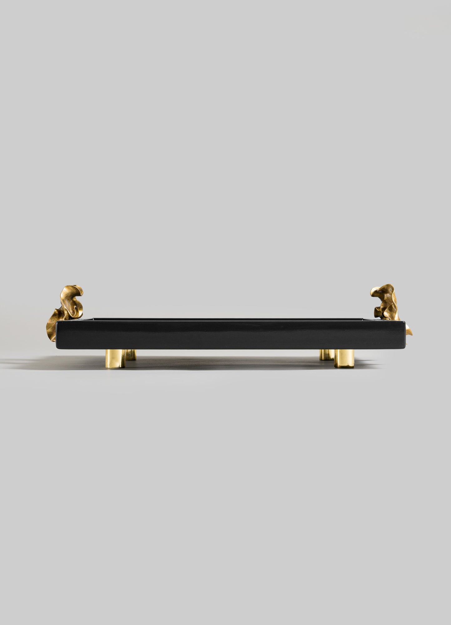 The VIYA Saffron Black Towel Tray features a sleek black rectangular design with gold animal figurines at two corners and four short gold legs, inspired by contemporary bronzed art, displayed on a plain light gray background.