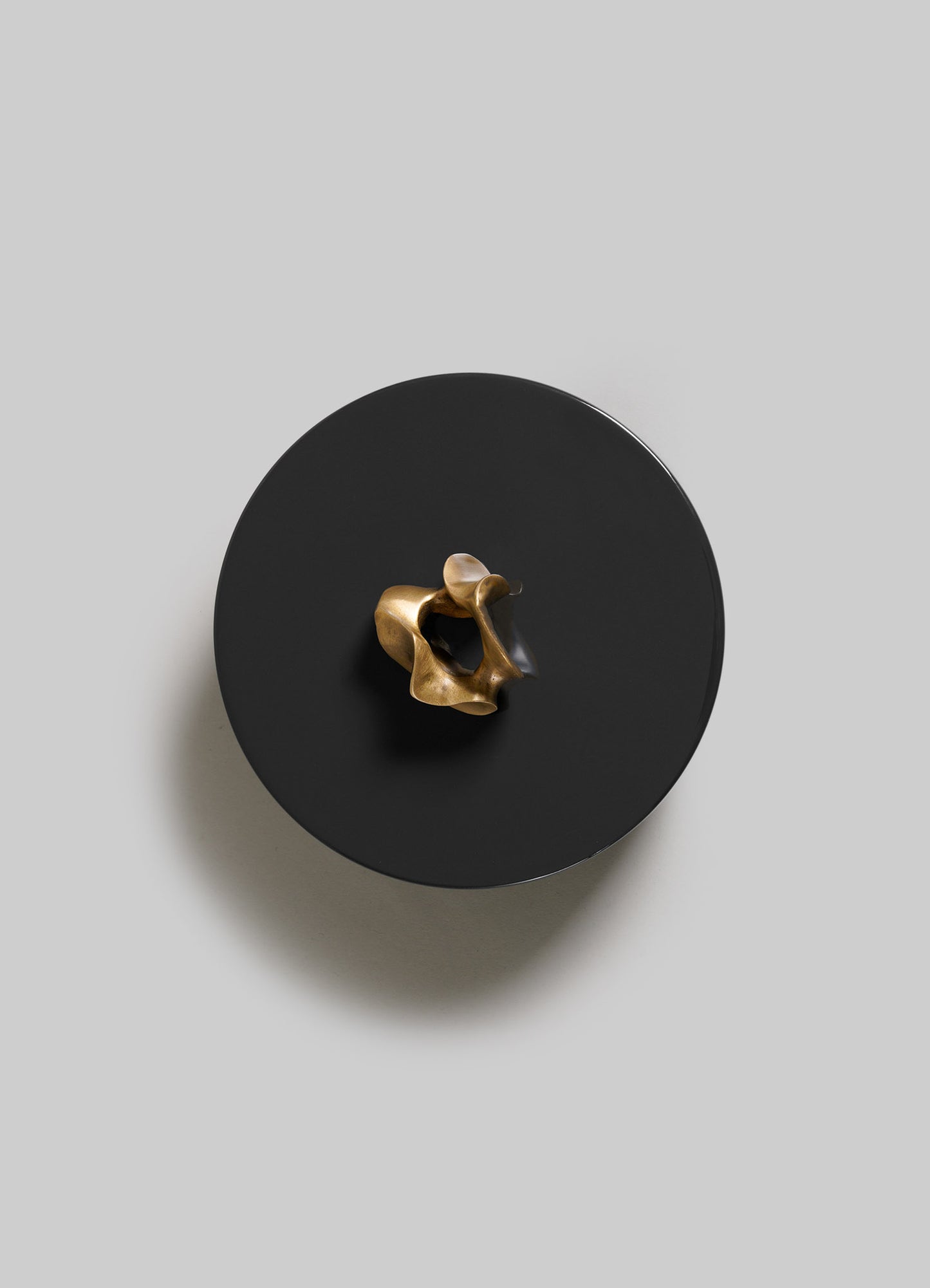 The VIYA Saffron Black Trinket Box Large features a small, abstract gold sculpture at its center on a round, flat black surface, viewed from above against a light gray background with a soft shadow to the left.