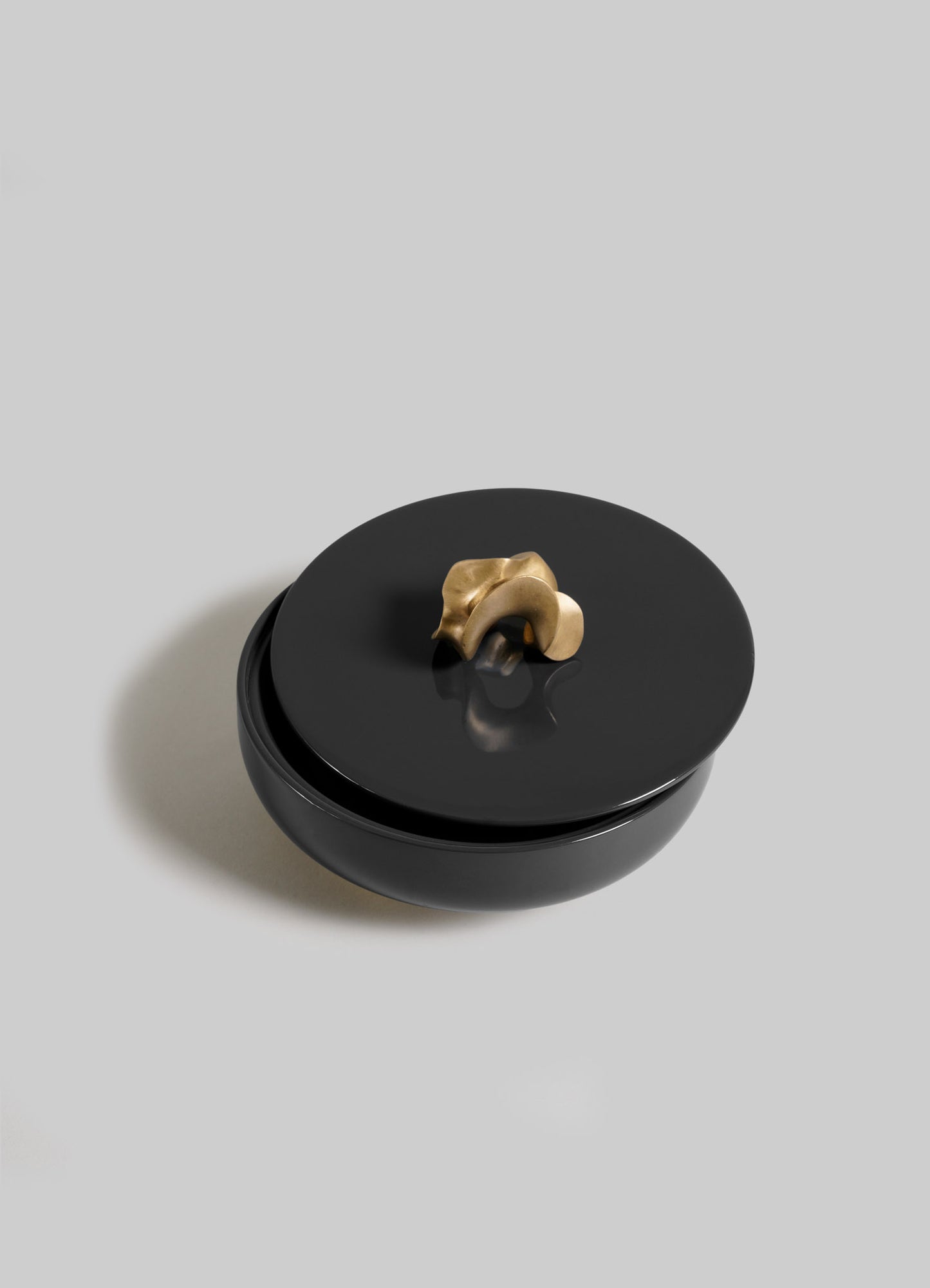 The VIYA Saffron Black Trinket Box Large is a round, glossy black container with a matching lid and small abstract gold handle, exuding elegance as it sits against a plain light gray background.