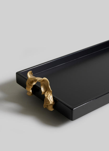 The VIYA Saffron Black Vanity Tray is a black rectangular tray with gold abstract handles, inspired by ancient Indian medicine and saffron threads, displayed on a light gray background.