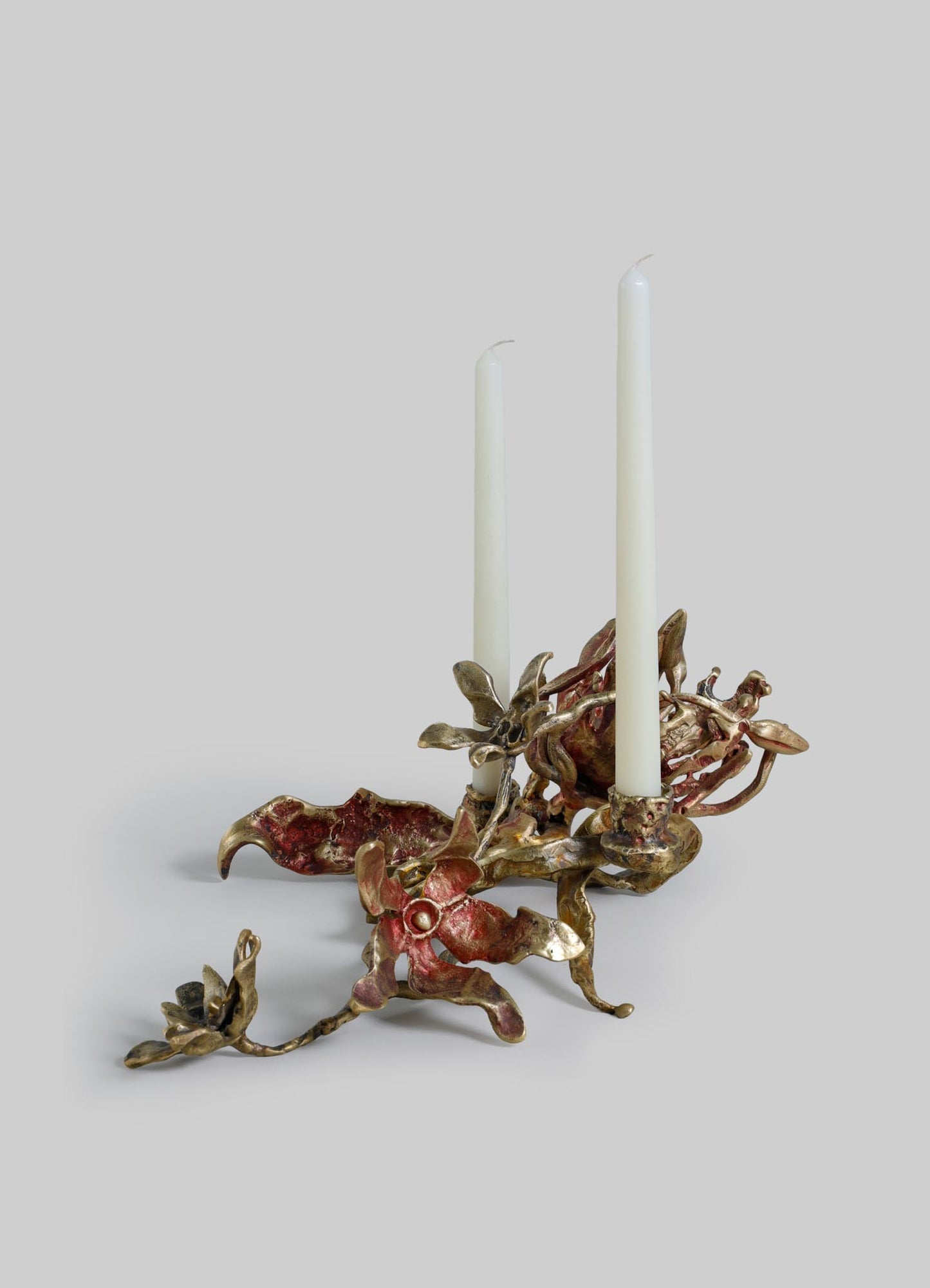 A decorative candle holder made of metal with a twisted, organic design resembling coral or natural forms, finished in a bronze or antique gold tone, holding two white tapered candles.