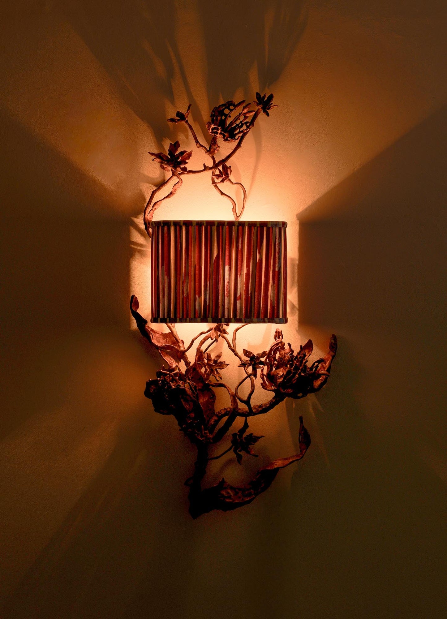 The VIYA Spring In Kashmir Wall Sconce A features a patina finish, cylindrical ribbed shade, and artistic metal branches and leaves—casting warm, dramatic light perfect for elevating your Kashmir-inspired home decor.