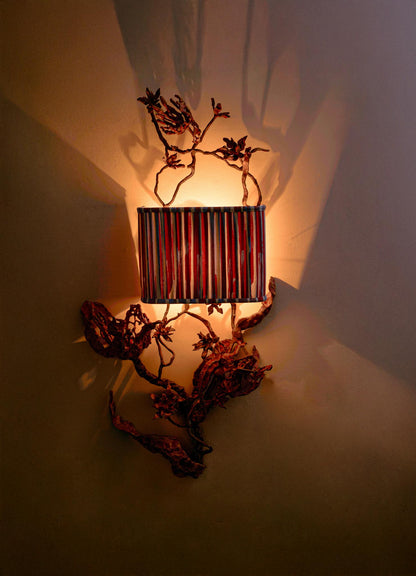The VIYA Spring In Kashmir Wall Sconce B features a striped lampshade and metal branches in brass and bronze tones, casting warm light and artistic shadows for an elegant touch inspired by Kashmir.