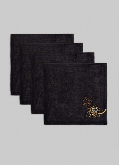 The Viya Tree Full of Parrots Hand Embroidered Black & Gold Cocktail Napkins (set of 4) feature intricate designs symbolizing blessings and good fortune, shown staggered atop a light gray background.