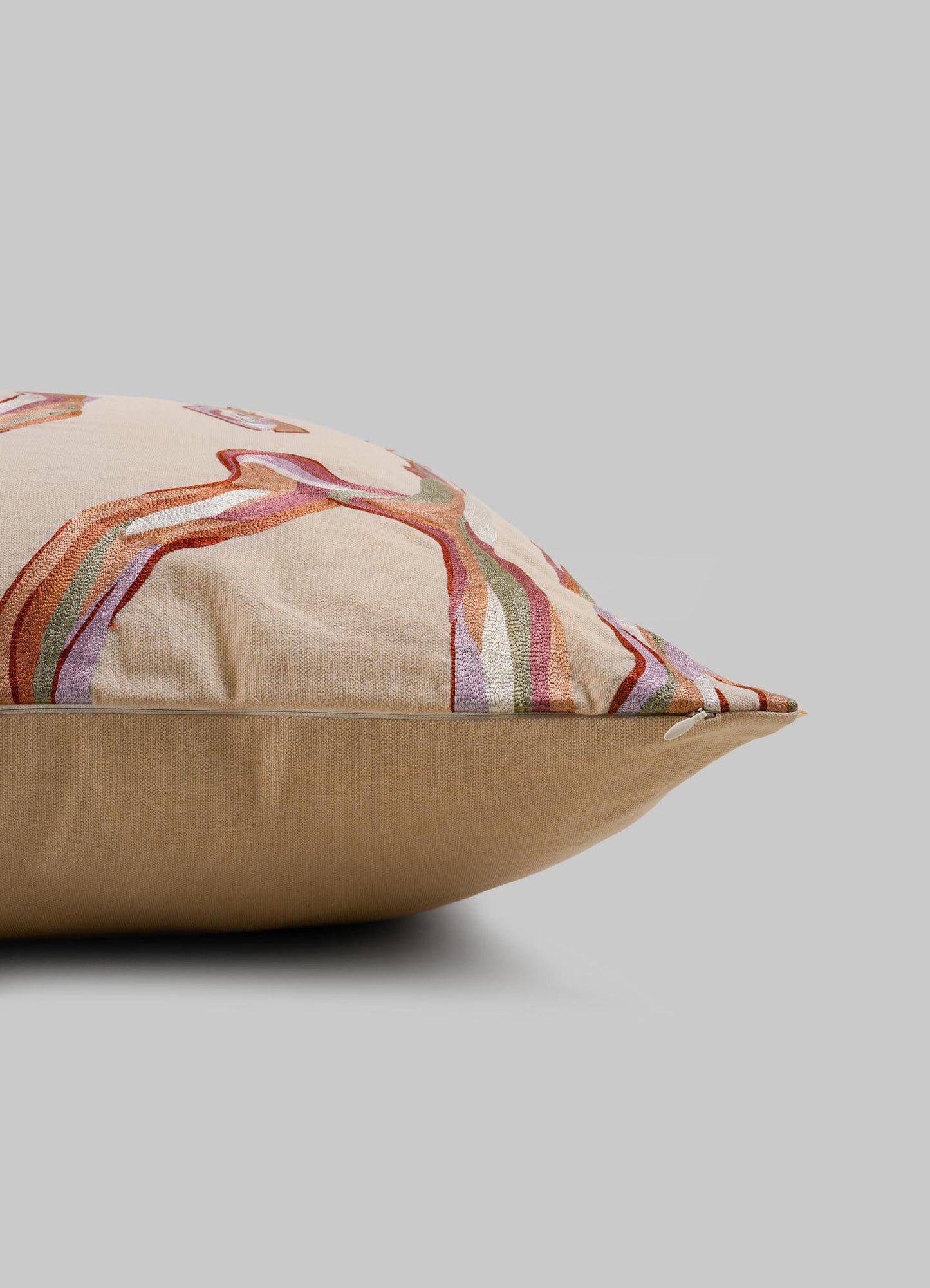 The Viya Tutti Frutti Salmon Pink Cushion Cover (24"x24") features multicolored abstract embroidery inspired by hand-embroidered cushions, shown from a side angle against a plain gray background.