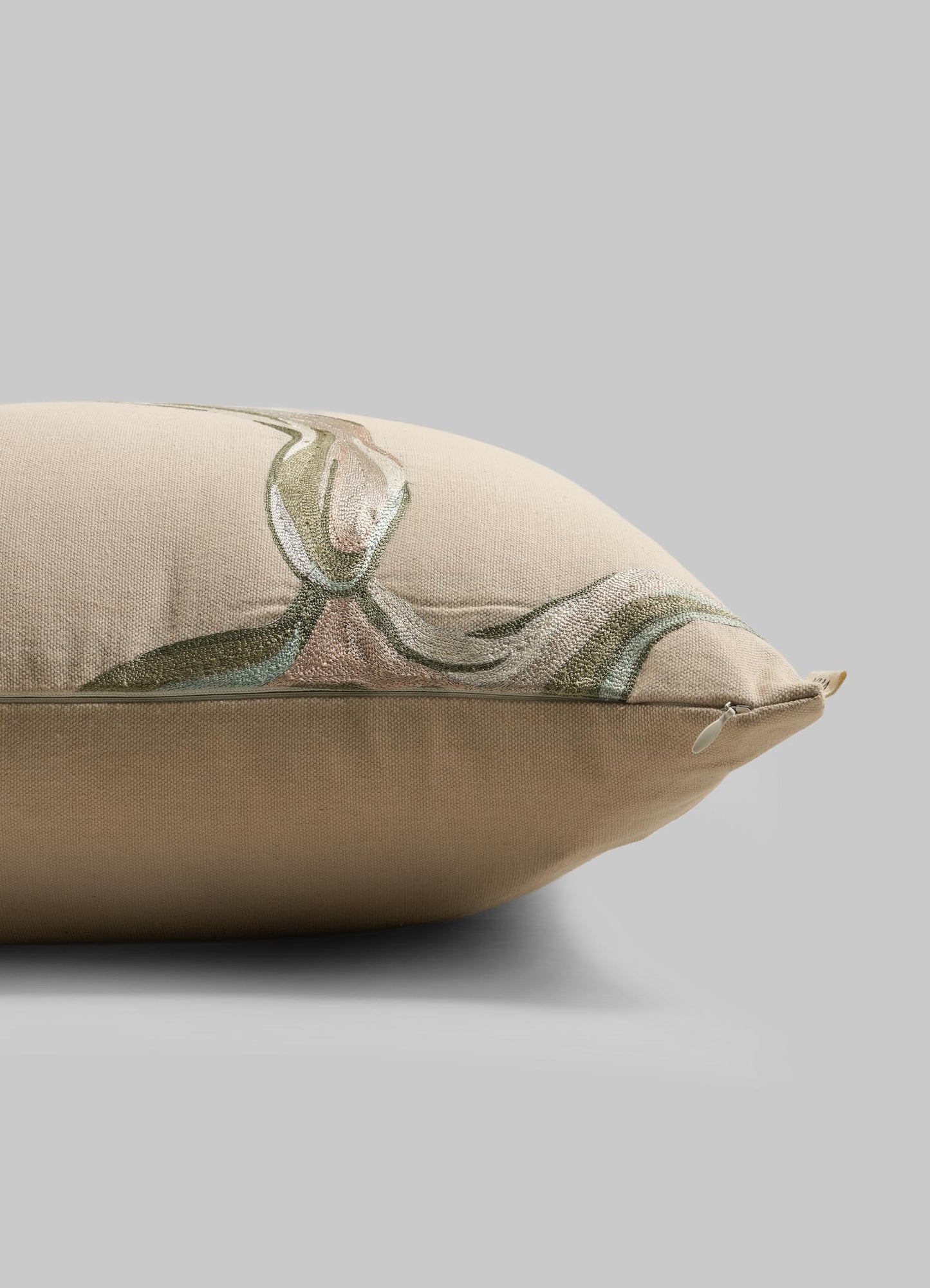 The Viya Tutti Frutti Sea Green Cushion Cover 18"x18" features a subtle, abstract design in muted green, brown, and cream tones, inspired by hand-embroidered cushions. Shown on its side with a visible zipper against a light gray background.